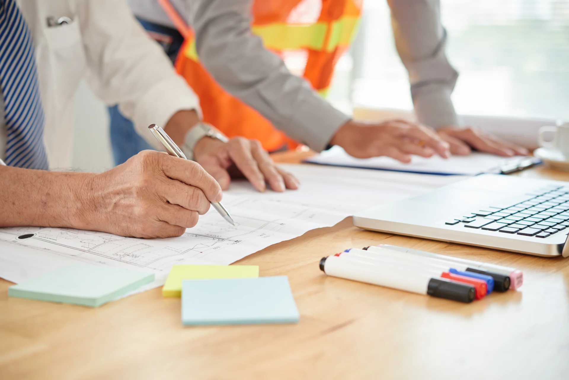 Architekten und Bauleiter prüfen Pläne mit Notizen und Markierungen am Tisch