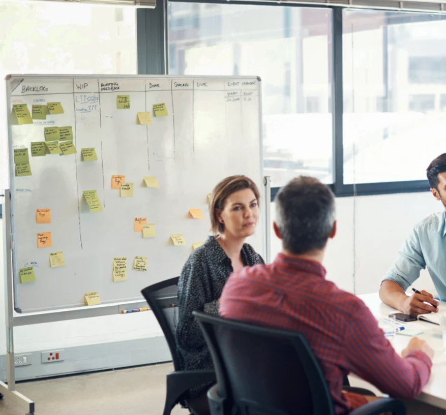 Drei Personen bei einer Teambesprechung vor einem Whiteboard mit Kanban-Workflow und vielen Haftnotizen – 4D Bauprojekte GmbH, Daniel Wirth.